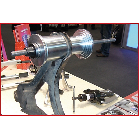 Ein Werkzeug zur Reparatur eines Fahrzeugs, das auf einem Tisch steht. In der Mitte befindet sich ein silberner Zylinder, der von einer schwarzen Halterung getragen wird.